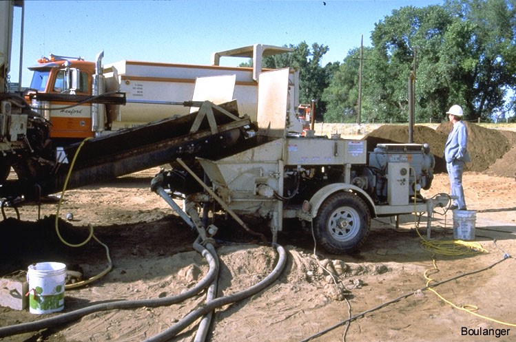 A grout pump with lines running to grout pipes. The silty sand material used in grout mix can be seen in the background.<br />(Courtesy of Dr. Ross Boulanger, UC Davis).